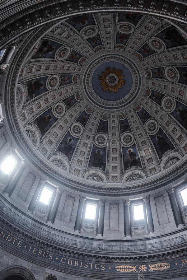 Captivating interior of a grand domed cathedral with Latin inscriptions, radiant centerpieces, and statues in niches, bathed in natural light from large windows. Location unspecified. Captivating interior of a grand domed cathedral with Latin inscriptions, radiant centerpieces, and statues in niches, bathed in natural light from large windows. Location unspecified.