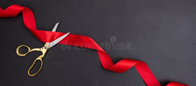 Grand opening. Top view of gold scissors cutting red silk ribbon against black background, banner