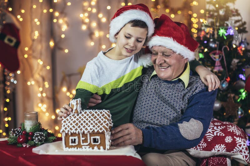 Grand-père et petit-fils assis sur la chaise avec la maison en pain d'épices pendant noël photo stock