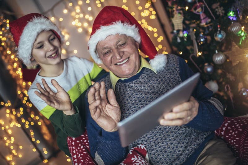 Grand-père et petit-fils assis sur la chaise et regardant la tablette numérique pendant noël. image libre de droits