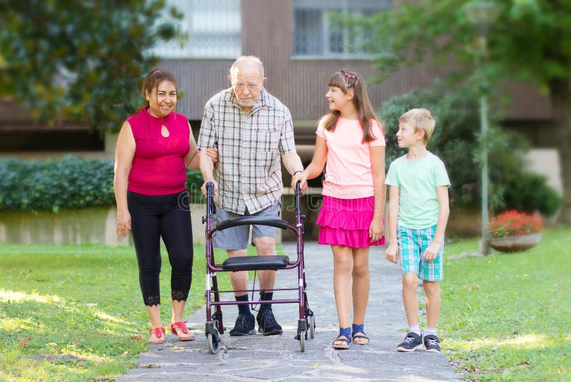Grandchildren and caregiver accompanies their grandfather to walk helping him stock photos.