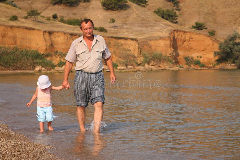 Grandfather with granddaughter goes as to water on beach. Grandfather with granddaughter goes as to water on beach