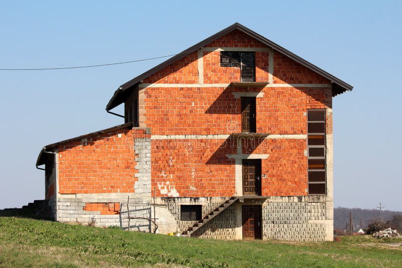 Grande casa suburbana inacabado da fam?lia do tijolo vermelho no lado do monte pequeno cercado com grama sem cortes fotografia de stock royalty free Grande casa suburbana inacabado da fam?lia do tijolo vermelho no lado do monte pequeno cercado com grama sem cortes fotografia de stock royalty free