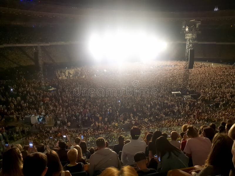 Grande folla dei fan che si siede sulle tribune dello stadio e che ascolta il concerto di musica rock alla notte Luce intensa e l immagini stock Grande folla dei fan che si siede sulle tribune dello stadio e che ascolta il concerto di musica rock alla notte Luce intensa e l immagini stock