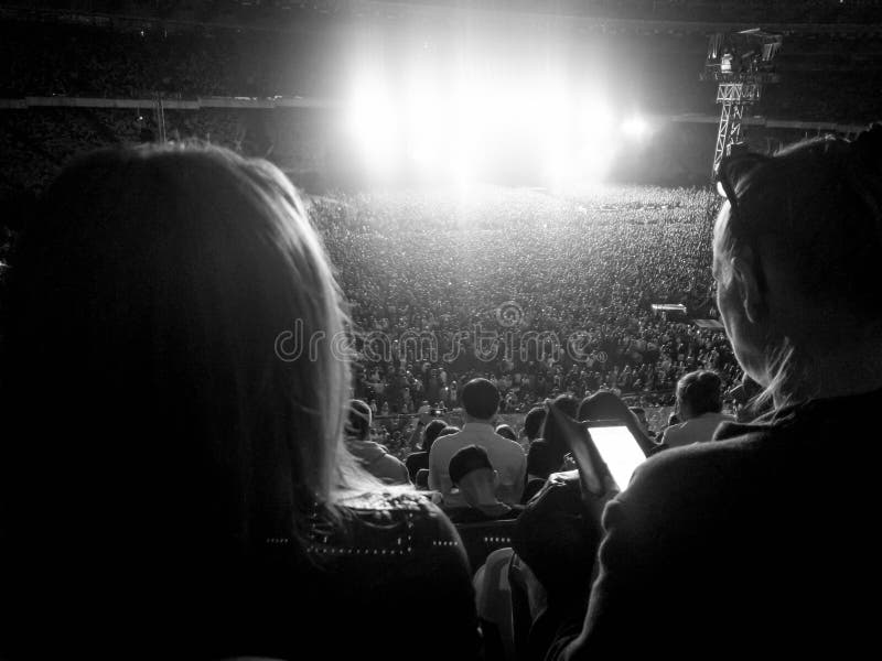 Grande folla dei fan che si siede sulle tribune dello stadio e che ascolta il concerto di musica rock alla notte Luce intensa e l fotografia stock libera da diritti Grande folla dei fan che si siede sulle tribune dello stadio e che ascolta il concerto di musica rock alla notte Luce intensa e l fotografia stock libera da diritti