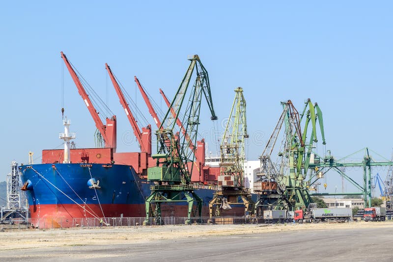 Grande nave da carico blu del Mar Rosso mentre parcheggiando nel porto Le gru del porto scaricano il carico nella nave Il lavoro fotografia stock libera da diritti Grande nave da carico blu del Mar Rosso mentre parcheggiando nel porto Le gru del porto scaricano il carico nella nave Il lavoro fotografia stock libera da diritti