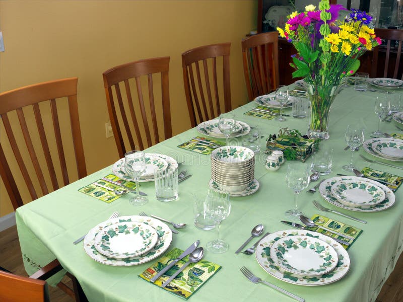 Table for 12 people with light green tablecloth and beautiful porcelain service waiting for the guests to arrive. Colorful bouquet in the center. Table for 12 people with light green tablecloth and beautiful porcelain service waiting for the guests to arrive. Colorful bouquet in the center