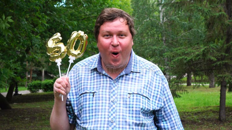 Grande uomo che tiene i palloni dorati che rendono il numero 50 all'aperto cinquantesimo partito di celebrazione di anniversario