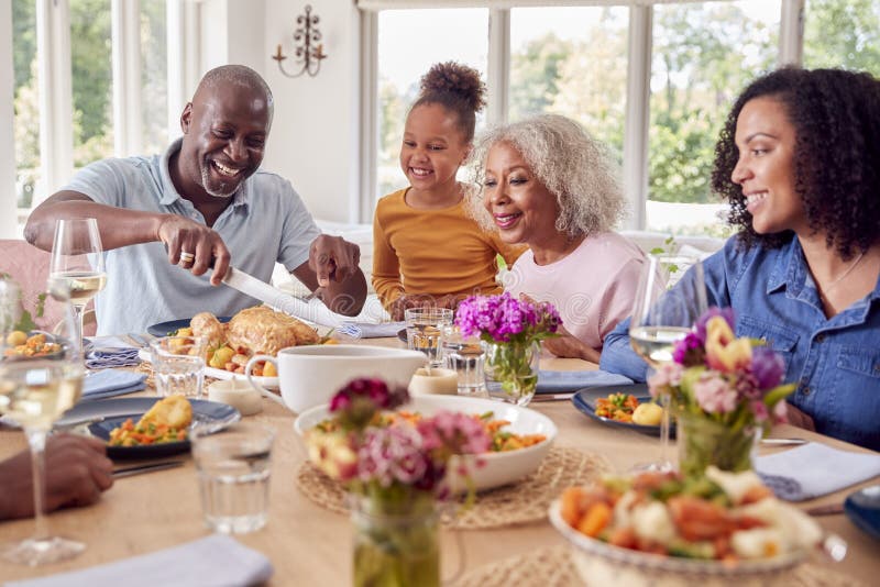 Grandfather Carving As Multi Generation Family Sit Around Table at Home ...