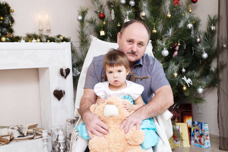 Grandfather and granddaughter portrait in Christmas interior. Little girl sitting behind older father with Teddy bear royalty free stock photography Grandfather and granddaughter portrait in Christmas interior. Little girl sitting behind older father with Teddy bear royalty free stock photography