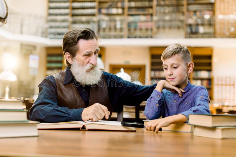 Grandfather his grandson, teacher and student, sitting at the table in ancient library, boy is interested in reading royalty free stock image