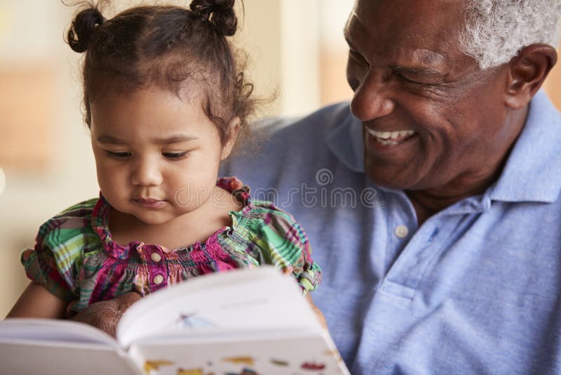 Grandfather Sitting On Sofa At Home With Baby Granddaughter Reading Book Together royalty free stock images Grandfather Sitting On Sofa At Home With Baby Granddaughter Reading Book Together royalty free stock images