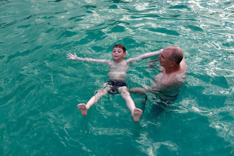 Grandfather teaches grandson to swim on his back in thermal pool stock photography