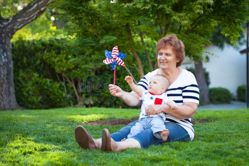 Grandmother and baby boy playing with a pinwheel on a green lawn