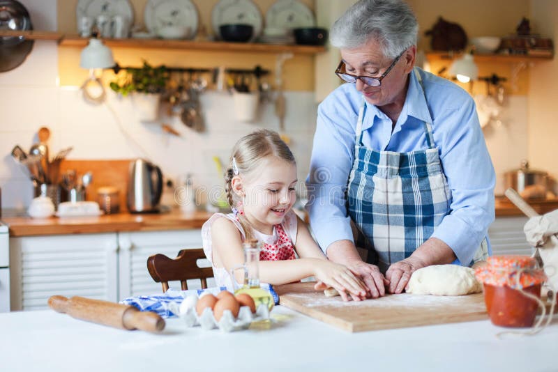 Grandmother is teaching child to cook in cozy home kitchen. Senior woman and little girl are smiling. royalty free stock images Grandmother is teaching child to cook in cozy home kitchen. Senior woman and little girl are smiling. royalty free stock images