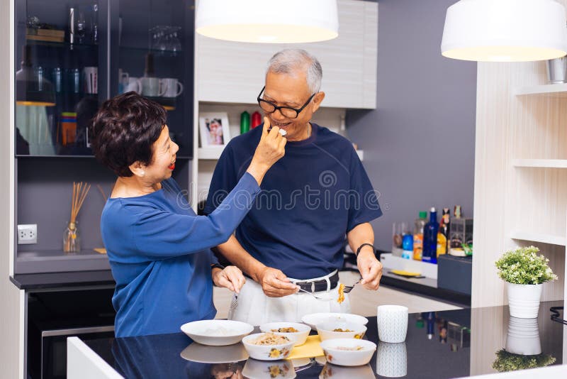 Grands-parents asiatiques supérieurs de couples faisant cuire ensemble tandis que la femme alimente la nourriture à l'homme à la photos stock Grands-parents asiatiques supérieurs de couples faisant cuire ensemble tandis que la femme alimente la nourriture à l'homme à la photos stock