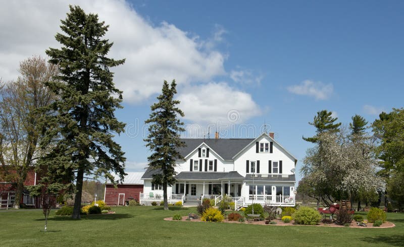 Big, large rural country farmhouse home on an old Wisconsin dairy farm. You can see some of the smaller barns in the image. The house is painted white and the sky is blue with clouds. Big, large rural country farmhouse home on an old Wisconsin dairy farm. You can see some of the smaller barns in the image. The house is painted white and the sky is blue with clouds.