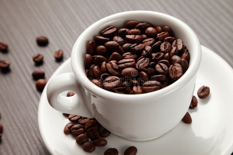 Granos de café en una taza, colocándose en una tabla de madera Granos de café de un alto nivel de asación