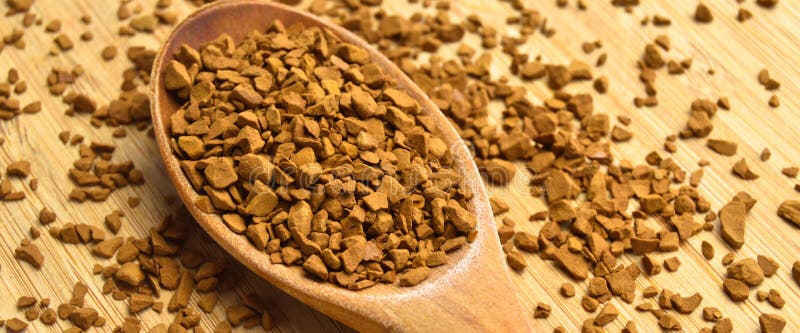 Granuli freschi di chicchi istantanei di caffè in cucchiaio di legno su fondo di bambù di legno