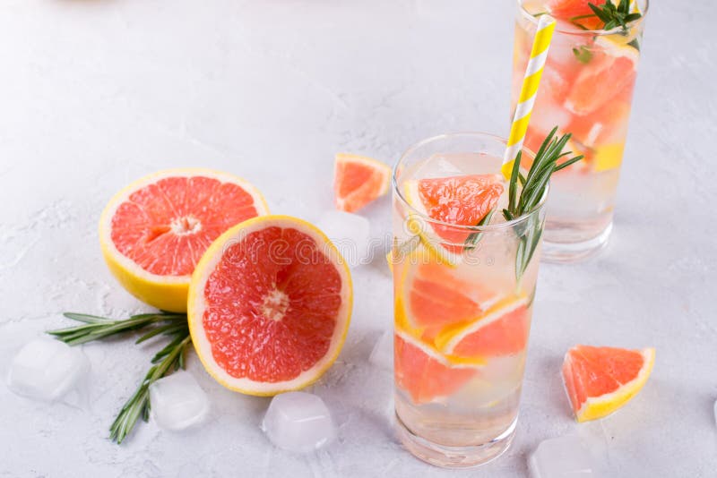 Grapefruit lemonade. Two glasses of refreshing drink, water with grapefruit, rosemary branches and ice. Recipe concept