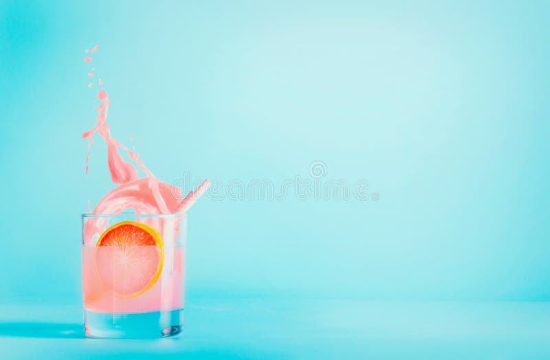 Grapefruktdrink i exponeringsglas med färgstänk på blå bakgrund Uppfriskande dryck f?r sommar Lemonad för rosa grapefrukt kopiera arkivbilder Grapefruktdrink i exponeringsglas med färgstänk på blå bakgrund Uppfriskande dryck f?r sommar Lemonad för rosa grapefrukt kopiera arkivbilder