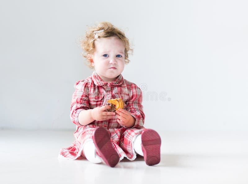 Grappig babymeisje die rode kleding dragen die Kerstmispastei eten royalty-vrije stock foto Grappig babymeisje die rode kleding dragen die Kerstmispastei eten royalty-vrije stock foto