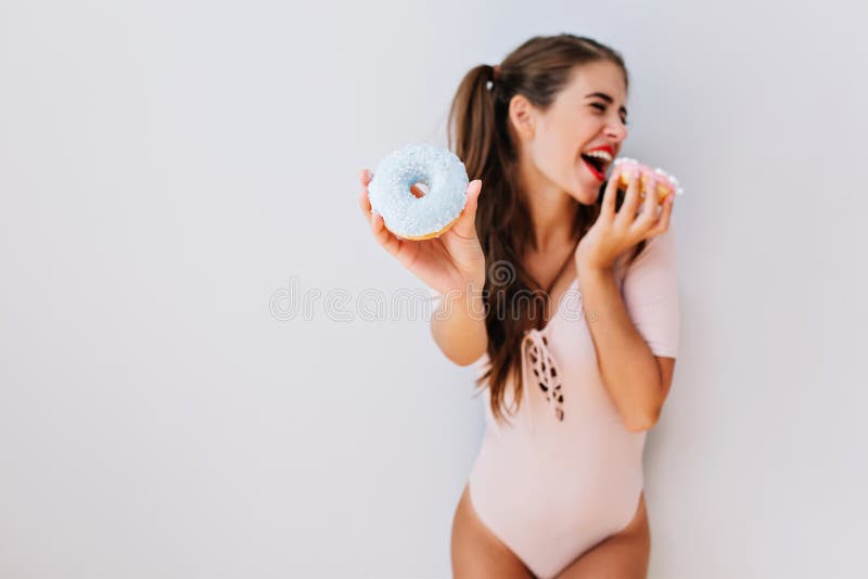 Grappig jong mooi meisje met lang haar in roze bodysuit die pret met kleurrijke donuts hebben Blije jonge vrouw met slank royalty-vrije stock afbeeldingen Grappig jong mooi meisje met lang haar in roze bodysuit die pret met kleurrijke donuts hebben Blije jonge vrouw met slank royalty-vrije stock afbeeldingen