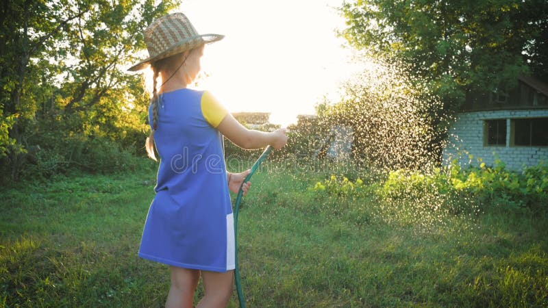 Grappig klein meisje in hoed met tuinslang in de zonnige achtertuin. heerlijk klein meisje dat met een tuinslang speelt
