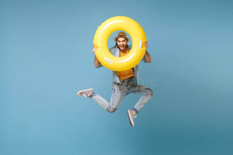 Funny traveler tourist man in yellow casual summer clothes isolated on blue background. Male passenger traveling abroad to travel on weekends. Air flight journey concept. Jumping hold inflatable ring. Funny traveler tourist man in yellow casual summer clothes isolated on blue background. Male passenger traveling abroad to travel on weekends. Air flight journey concept. Jumping hold inflatable ring