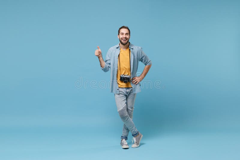 Funny traveler tourist man in yellow summer casual clothes with photo camera isolated on blue background. Male passenger traveling abroad on weekends. Air flight journey concept. Showing thumb up. Funny traveler tourist man in yellow summer casual clothes with photo camera isolated on blue background. Male passenger traveling abroad on weekends. Air flight journey concept. Showing thumb up