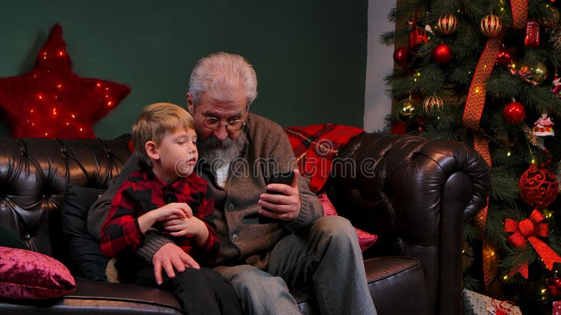 Graseninhalt des eleganten alten Mannes und der kleinen Jungen auf einem Smartphone und Haben Spaß. Großvater und Enkelsohn sitzen