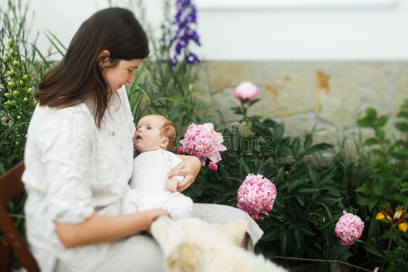 Grattis Mothers Day! Mor kramar sött nyfött barn bland blommor i trädgården. Kärleksvård och familj på landsbygden. arkivbilder