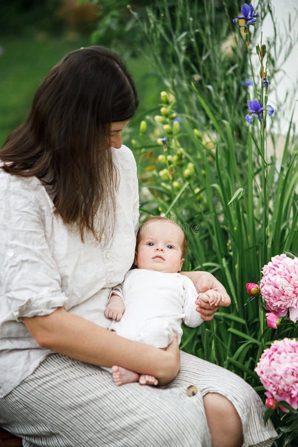 Grattis Mothers Day! Mor kramar sött nyfött barn bland blommor i trädgården. Kärleksvård och familj på landsbygden. fotografering för bildbyråer