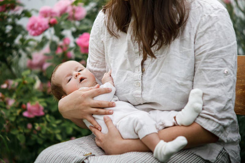 Grattis Mothers Day! Mor kramar sött nyfött barn bland blommor i trädgården. Kärleksvård och familj på landsbygden. arkivbild
