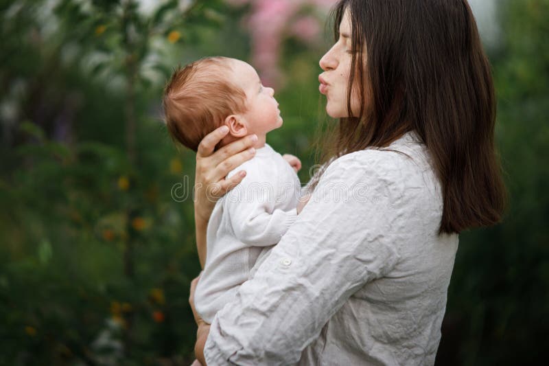 Grattis Mothers Day! Mor kysser och kramar söt nyfödd i trädgården. Kärleksvård och familj på landsbygden. arkivfoto