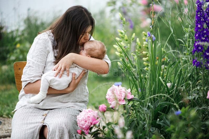 Grattis Mothers Day! Mor kysser och kramar sött nyfött barn bland blommor i trädgården. Kärleksvård och familj på landsbygden royaltyfri bild