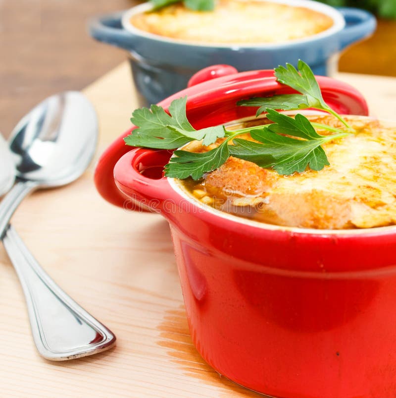 French Onion Soup Gratin in red and blue pots on table top. French Onion Soup Gratin in red and blue pots on table top
