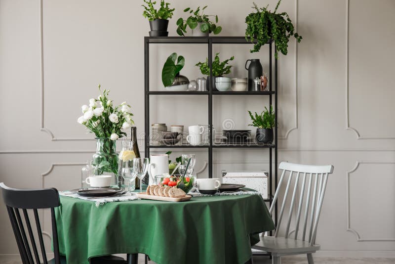 Grau und schwarze Holzstühle am Rundtisch mit grüner Tischdecke, Platten, Bechern und Weingläsern lizenzfreies stockfoto Grau und schwarze Holzstühle am Rundtisch mit grüner Tischdecke, Platten, Bechern und Weingläsern lizenzfreies stockfoto