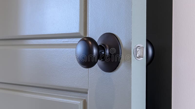 Panorama frame Gray paneled hinged wooden bedroom door with black door knob and visible latch. Close up view of a partially opened interior door with white doorframe. Panorama frame Gray paneled hinged wooden bedroom door with black door knob and visible latch. Close up view of a partially opened interior door with white doorframe.