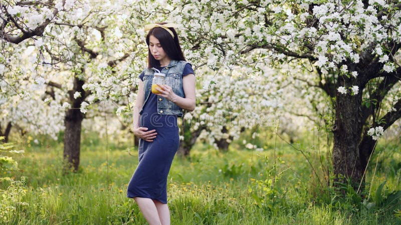 Gravid flicka som utomhus dricker orange fruktsaft