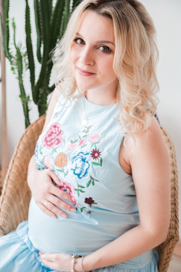 Gravid kvinna i en blå klänning som sitter i en vide- stol royaltyfria bilder Gravid kvinna i en blå klänning som sitter i en vide- stol royaltyfria bilder