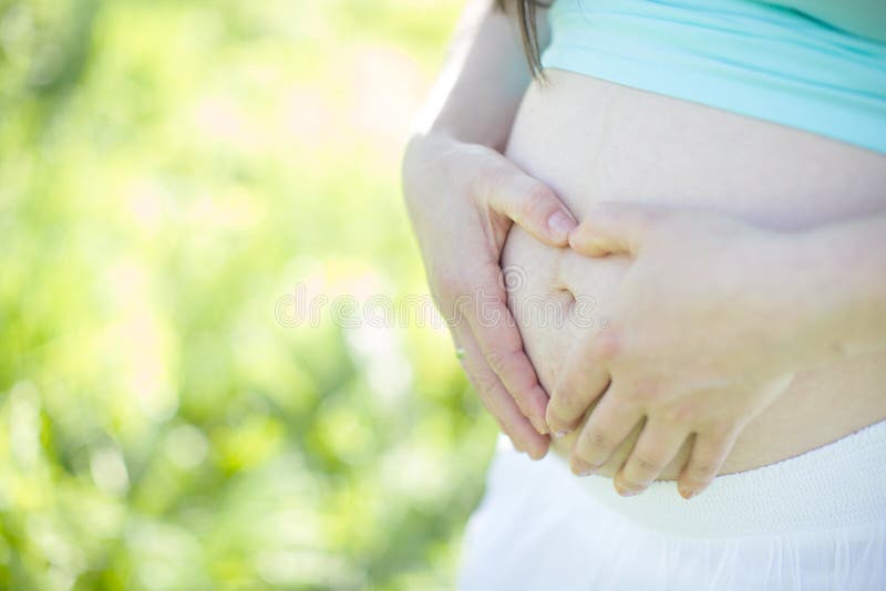 Gravid kvinna som omfamnar hennes buk och formar händer i en hjärta royaltyfri bild Gravid kvinna som omfamnar hennes buk och formar händer i en hjärta royaltyfri bild