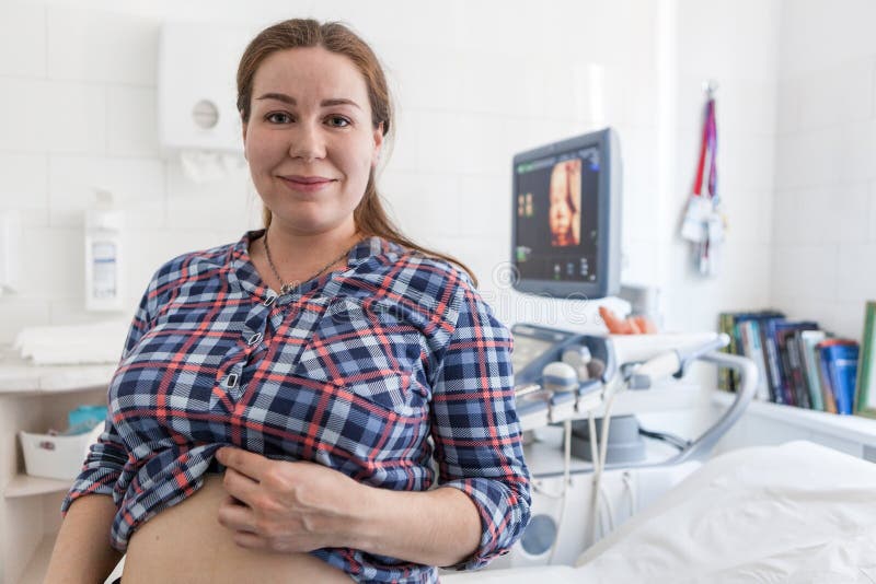Gravid kvinna som är lycklig med resultatet av ultraljudsundersökningen som står i sjukhusrum med modellen 3d av fostret på skärm arkivfoto Gravid kvinna som är lycklig med resultatet av ultraljudsundersökningen som står i sjukhusrum med modellen 3d av fostret på skärm arkivfoto