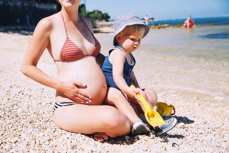 Gravid moder- och litet barnbarn som kopplar av på stranden på sommar royaltyfria foton Gravid moder- och litet barnbarn som kopplar av på stranden på sommar royaltyfria foton