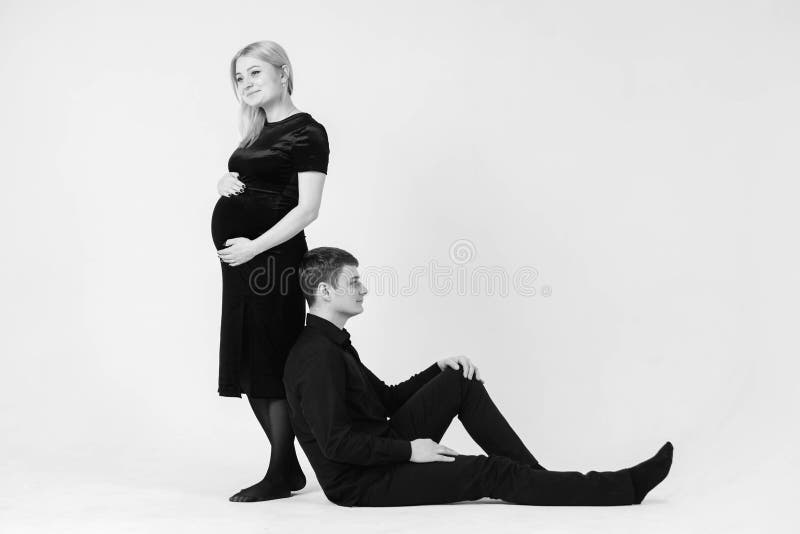 Gravida kvinnor och hennes make leende i svarta kläder på vit bakgrund Svartvit bild Vackert gifta par fotografering för bildbyråer
