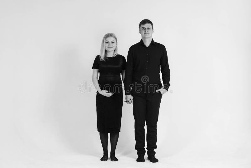 Gravida kvinnor och hennes make som håller händerna i svarta kläder på vit bakgrund Svartvit bild Snygg gift arkivbilder