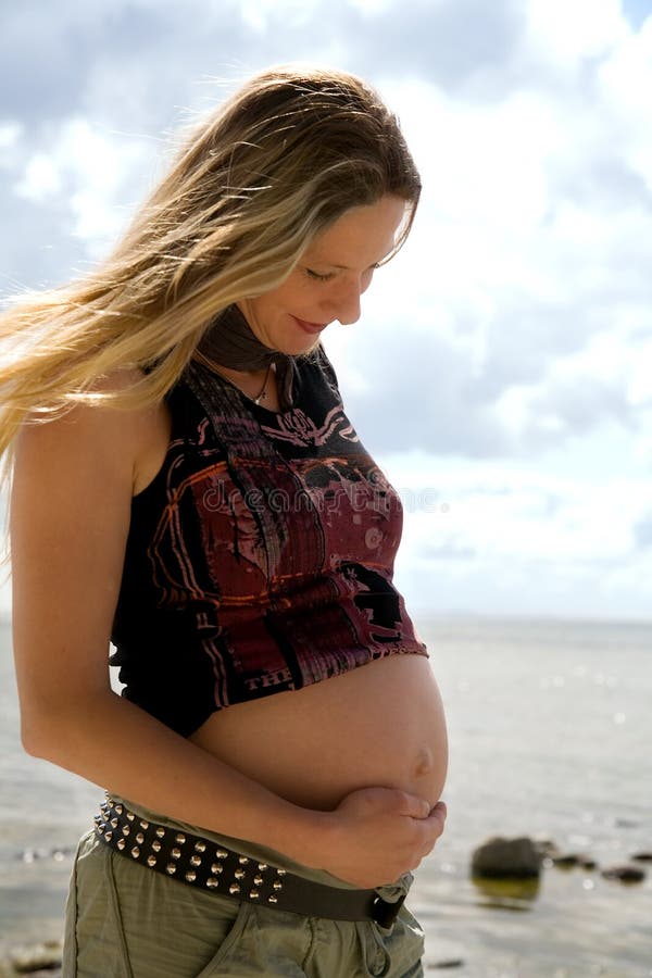 A young pregnant woman stands at the beach and feels the movements of the unborn child. A young pregnant woman stands at the beach and feels the movements of the unborn child