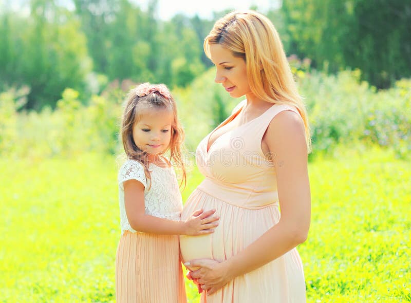 Gravidez e conceito de família - a mulher gravida feliz, filha da criança pequena toca na mãe da barriga no verão fotografia de stock Gravidez e conceito de família - a mulher gravida feliz, filha da criança pequena toca na mãe da barriga no verão fotografia de stock
