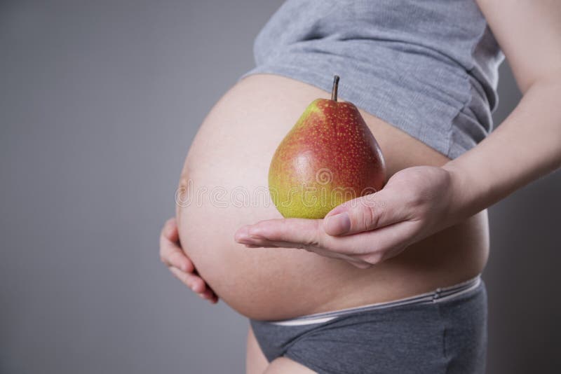 Gravidez e nutrição - mulher grávida com pera na mão sobre fundo cinzento imagem de stock royalty free