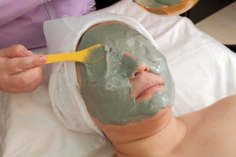 Gray alginate mask on the face of an Asian woman. The hands of a beautician put a lot on the face of the client. Skin lifting. stock photography Gray alginate mask on the face of an Asian woman. The hands of a beautician put a lot on the face of the client. Skin lifting. stock photography
